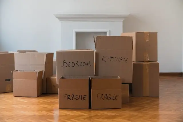 Organized moving boxes labeled with room names and fragile items stacked in empty room with hardwood floors