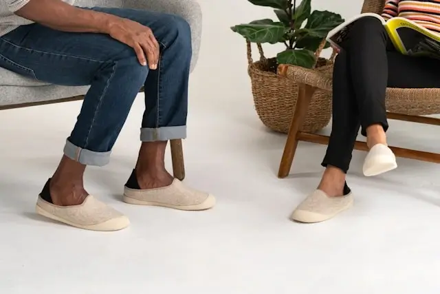 Two people wearing beige slip-on walking shoes while sitting, showing comfortable casual footwear options