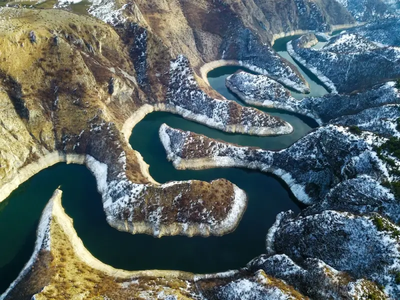 Aerial view of meandering river through snow-covered canyon landscape in Uvac River Canyon, showcasing dramatic terrain for whitewater rafting and adventure tourism