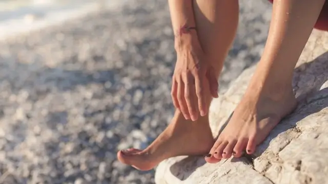 Person massaging bare foot while sitting on rock surface, highlighting foot comfort and care needs