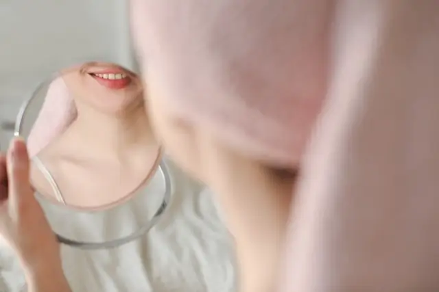 Person holding a round handheld mirror, showing their reflection with focus on lips and lower face area.