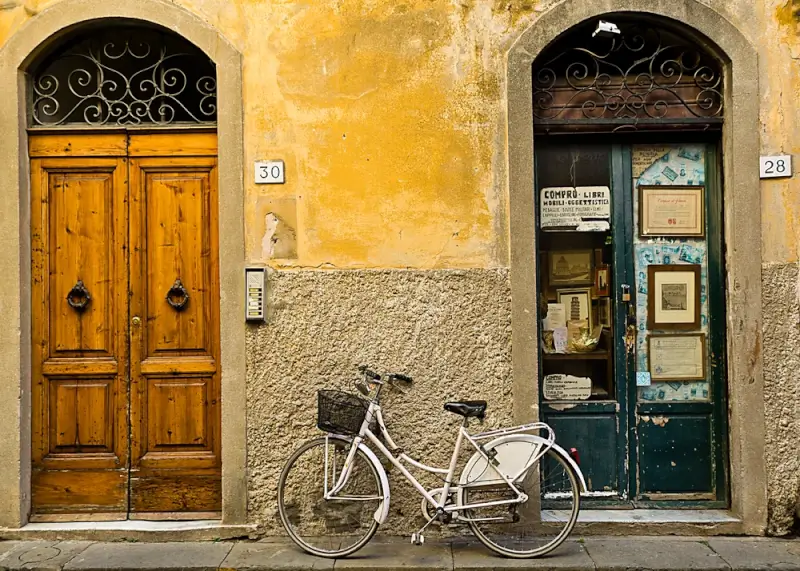 Traditional white bicycle parked on historic Italian street showcasing authentic cycling in Italy culture with weathered yellow facade and wooden doors
