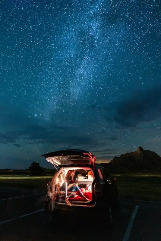 Car with open trunk parked on road under starry night sky during road trip camping adventure