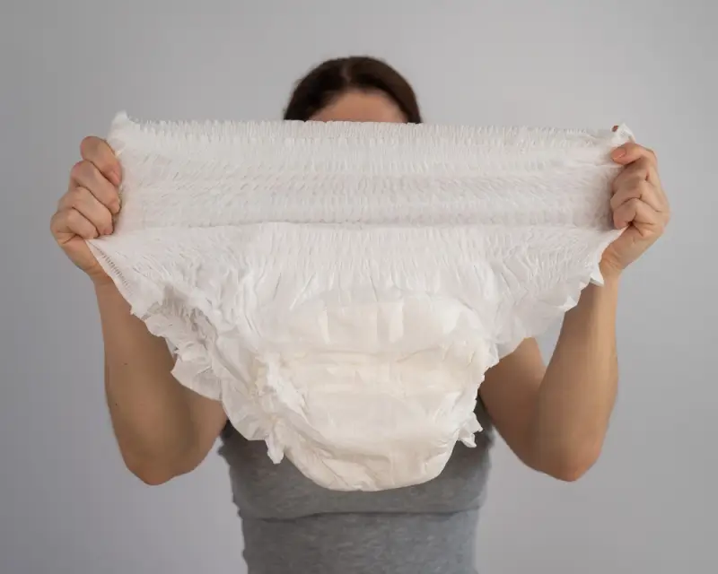 Woman holding white adult diaper showing absorbent core and elastic waistband for travel protection