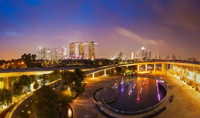 Singapore Marina Bay Sands casino resort skyline at sunset with illuminated fountains and Gardens by the Bay walkway in foreground