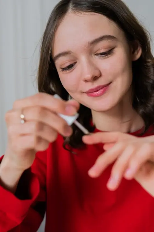Woman applying clear nail polish during at-home manicure wearing red sweater