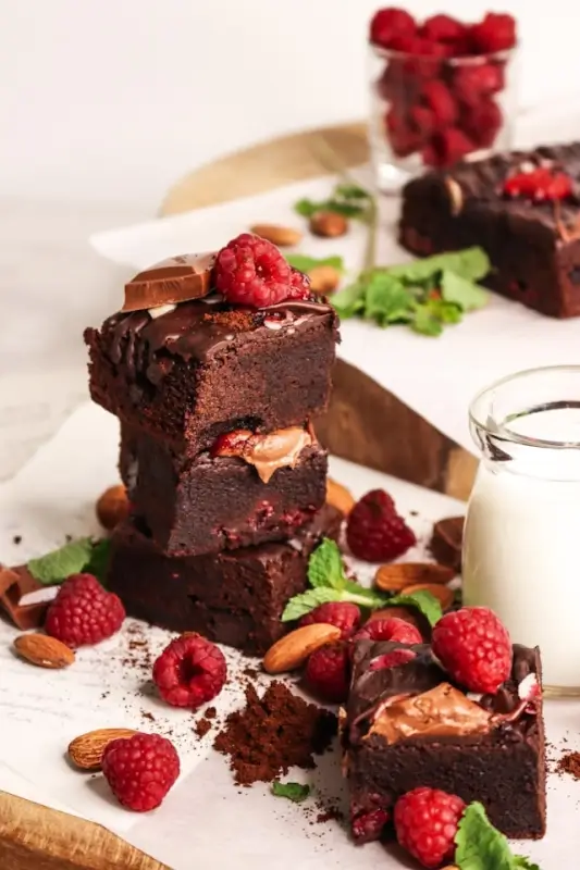 Stack of gourmet chocolate brownies with fresh raspberries, nuts and chocolate ganache topping, served with milk as birthday cake alternative