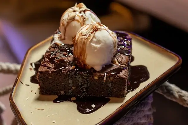 Decadent chocolate brownie slice topped with vanilla ice cream and caramel drizzle served as birthday dessert alternative to cake