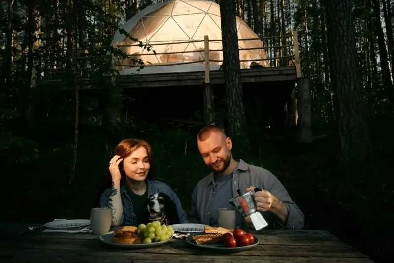 Long distance couple enjoying breakfast together at mountain cabin retreat with geodesic dome accommodation in forest background