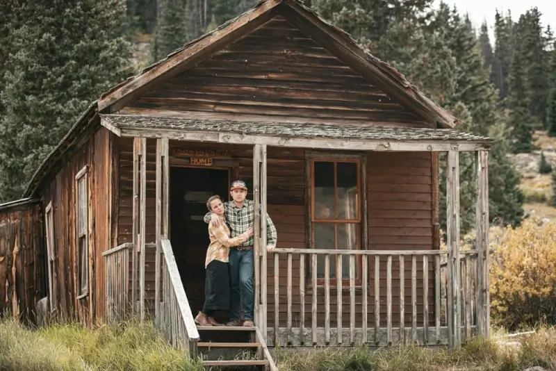 Long distance couple embracing on rustic mountain cabin porch surrounded by forest during romantic weekend getaway retreat