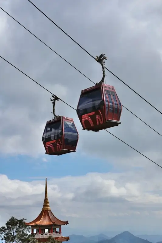 Red cable car gondolas suspended over mountain landscape with traditional Asian pagoda tower in Genting Highlands of Malaysia, representing scenic casino travel destinations