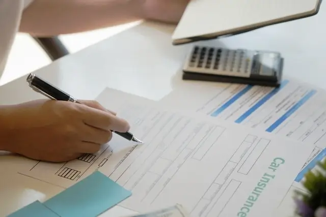 Person reviewing car insurance policy documents with calculator to compare coverage options and reduce insurance costs