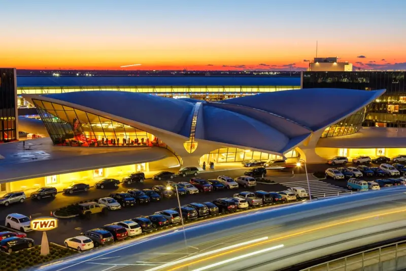 JFK airport terminal at sunset with cars and vehicles in pickup area showing busy transportation hub