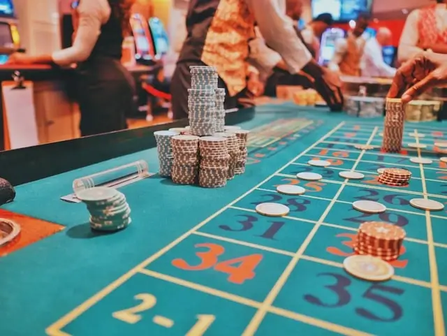Casino roulette table with stacked poker chips and players' hands placing bets on numbered green gaming surface