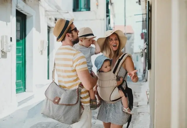 Digital nomad family with two young children exploring traditional white-washed Mediterranean village street while traveling together