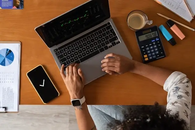 Person calculating timeshare costs and fees with laptop calculator and financial documents on desk