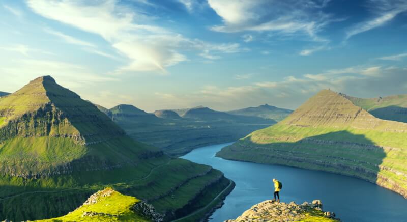 Hiker overlooking dramatic fjord and mountain landscape in Faroe Islands, showcasing Nordic natural beauty and hiking opportunities