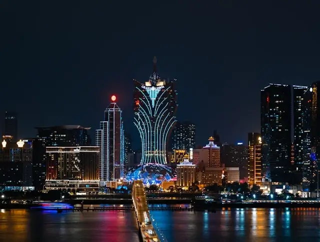 Macau casino skyline at night with illuminated Grand Lisboa tower and waterfront hotels reflecting in harbor waters