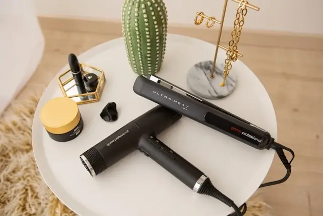 Hair styling tools including flat iron and hair dryer arranged on white table with decorative accessories