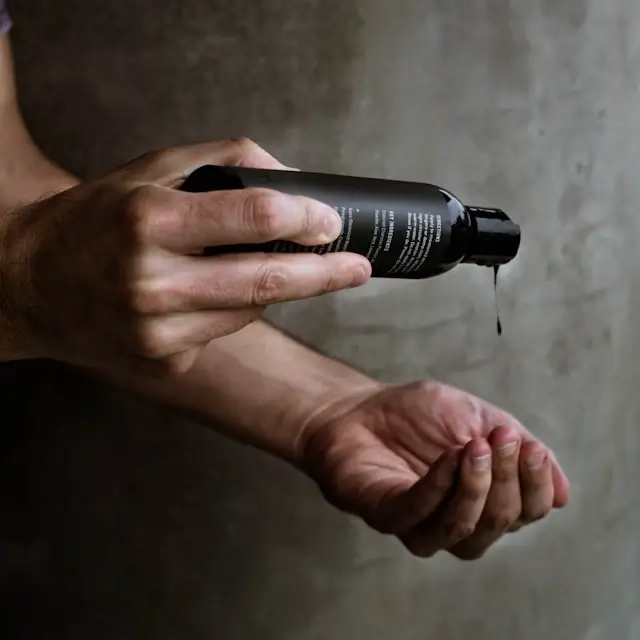 Hands dispensing hair care product from black bottle into palm for application