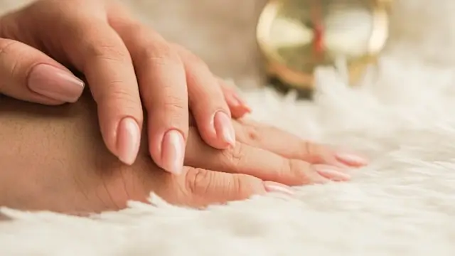 Hands with nude pink manicured nails resting on marble surface with skincare products