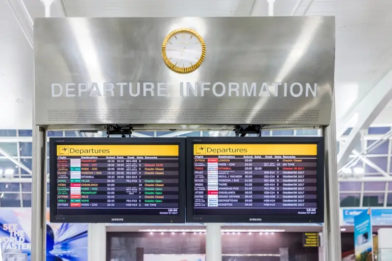 JFK airport departure information board displaying flight schedules and gate details with clock above