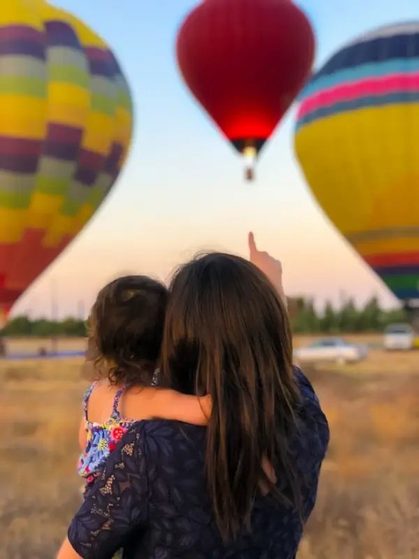 Digital nomad family watching colorful hot air balloons together, experiencing cultural adventures while traveling with kids