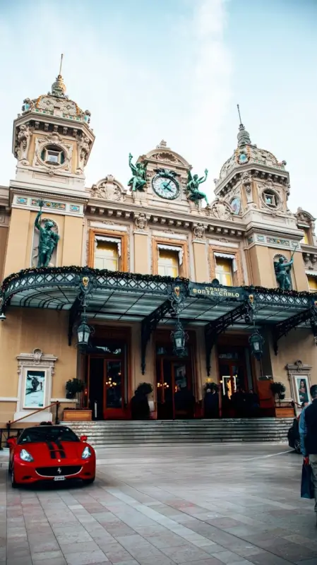 Monte Carlo Casino facade with ornate Belle Époque architecture, twin towers, and red Ferrari parked in front entrance plaza
