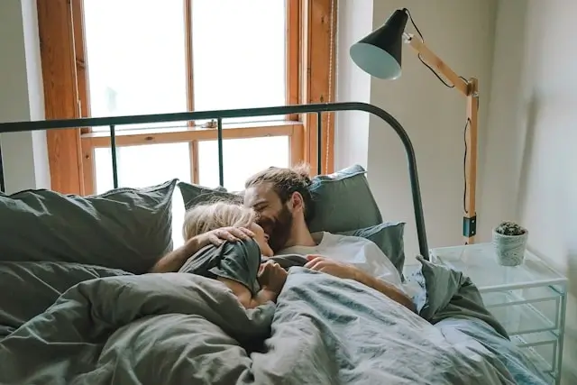 Intimate couple cuddling in comfortable bedroom environment with soft lighting, demonstrating emotional connection and bedroom confidence
