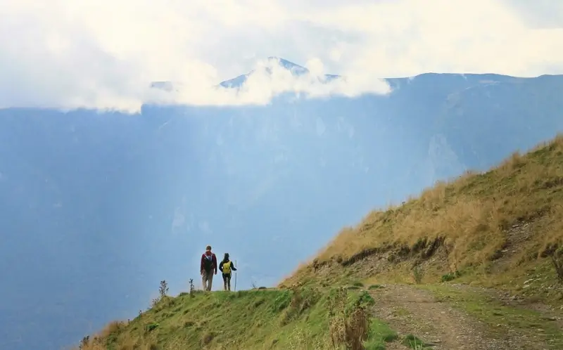 Long distance couple hiking together on mountain trail with dramatic valley views, building teamwork and emotional connection