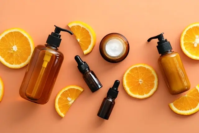 Natural hair care products in amber bottles with vitamin C rich orange slices on coral background