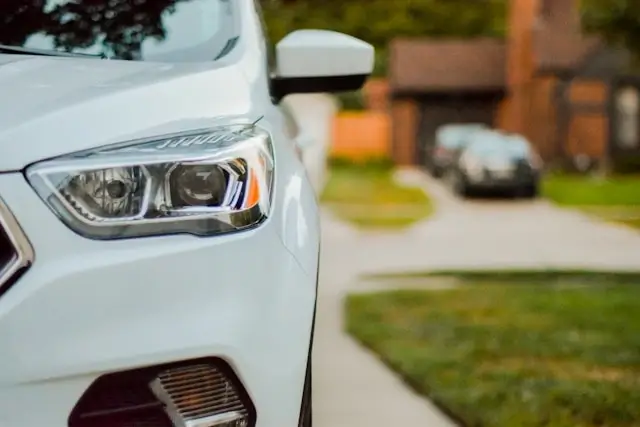 White car parked in residential driveway with modern LED headlights showing typical family vehicle needing standard car insurance