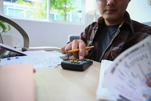 Payroll professional using calculator with financial documents and laptop for payroll processing tasks