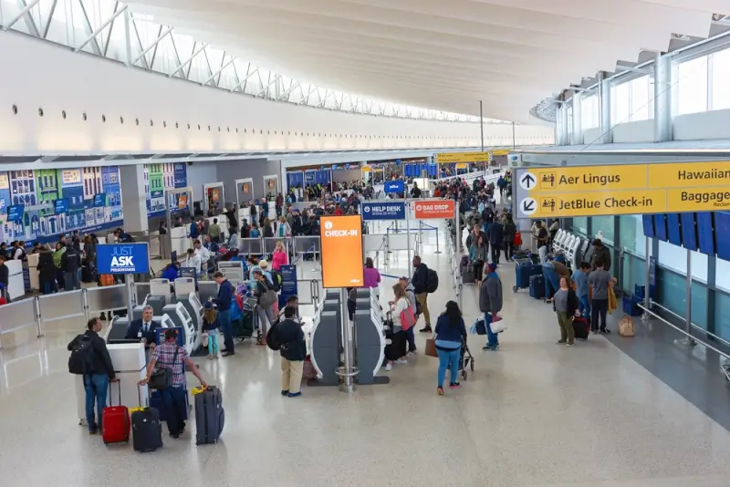 Busy JFK airport terminal interior with travelers and luggage at check-in counters and airline service desks