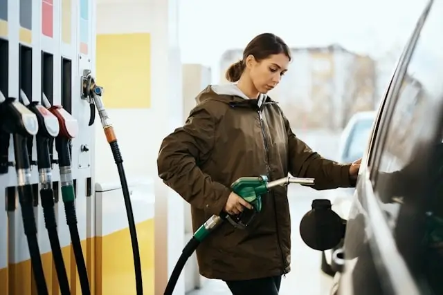 Woman refueling car with gasoline at gas station showing traditional fossil fuel dependency