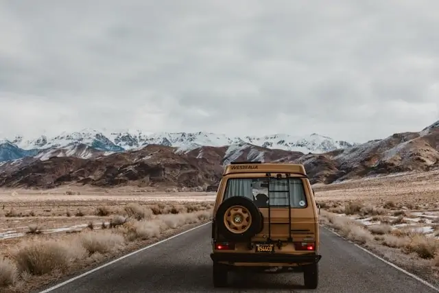 Yellow van driving on mountain highway with snow-capped peaks ahead during scenic road trip