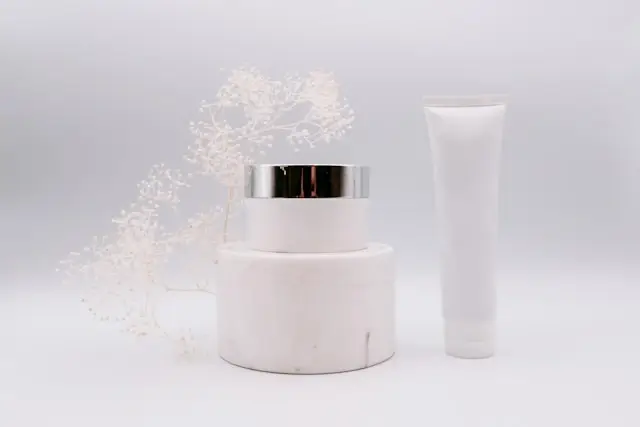 White private label skincare jar with silver cap and tube against minimalist background with dried flowers, demonstrating clean product branding