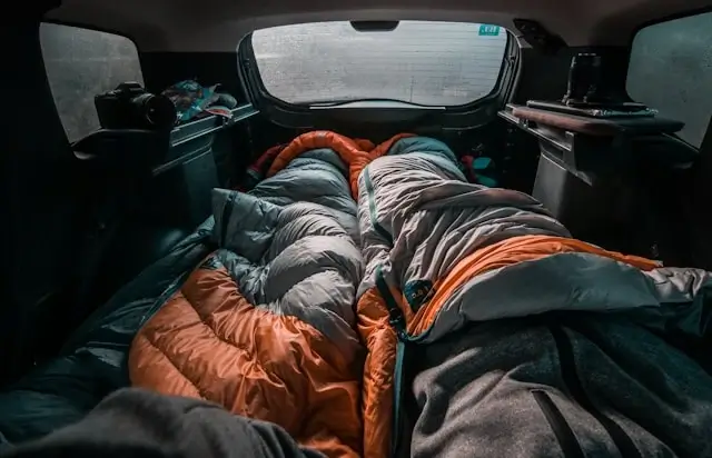 Travelers sleeping in sleeping bags inside car during road trip camping adventure