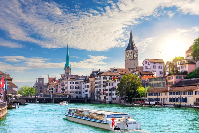 Historic Zurich waterfront with traditional Swiss architecture and tour boat on the Limmat River