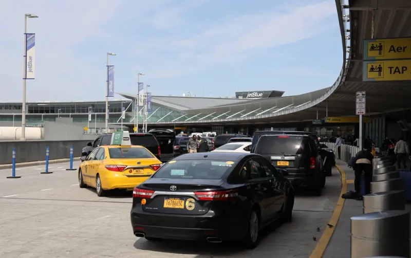 Cars and taxis waiting at JFK airport terminal pickup area with JetBlue signage visible overhead
