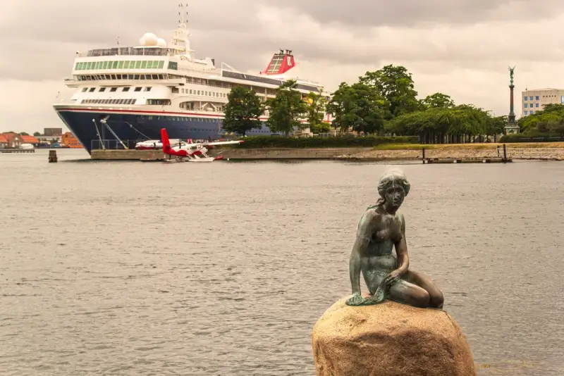 Famous Little Mermaid statue in Copenhagen harbor with cruise ship docked in background, highlighting Denmark's capital as a Northern Europe destination from Southampton UK cruises