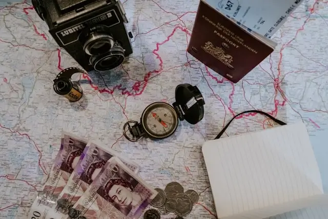 Travel planning essentials on map including passport, British pounds, compass, vintage camera and white shopping bag for casino travel budgeting