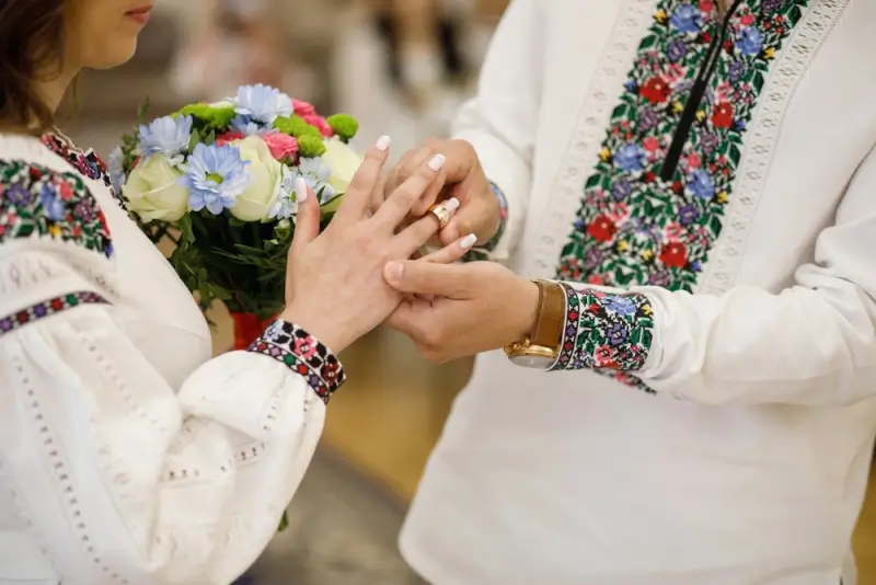 Ukrainian woman and man exchanging wedding rings in traditional embroidered clothing with floral bouquet