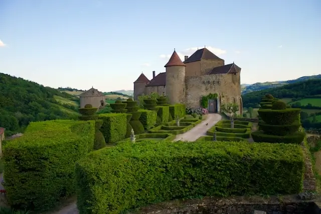 Historic French château with medieval stone towers and manicured topiary gardens set in rolling countryside, representing prestigious wine estates in Burgundy France