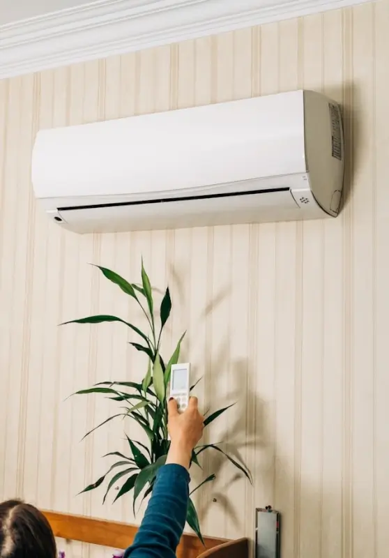 Person operating wall-mounted air conditioning unit with remote control in modern home interior