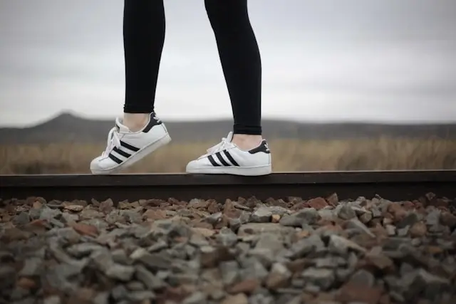 Close-up of legs in black cotton leggings and white striped sneakers balancing on railroad track