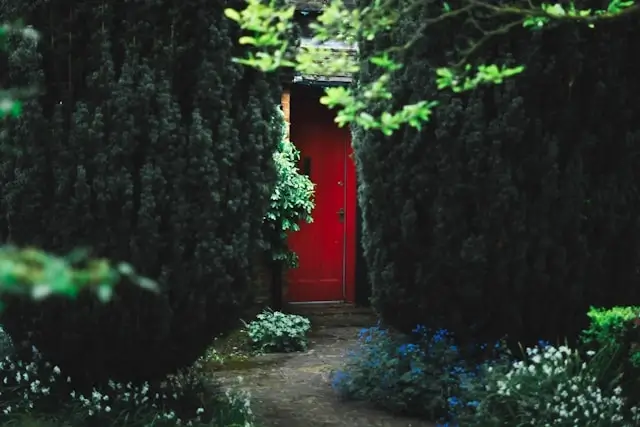 Red door garden pods entrance surrounded by lush green foliage and flowering plants creating a private backyard retreat space