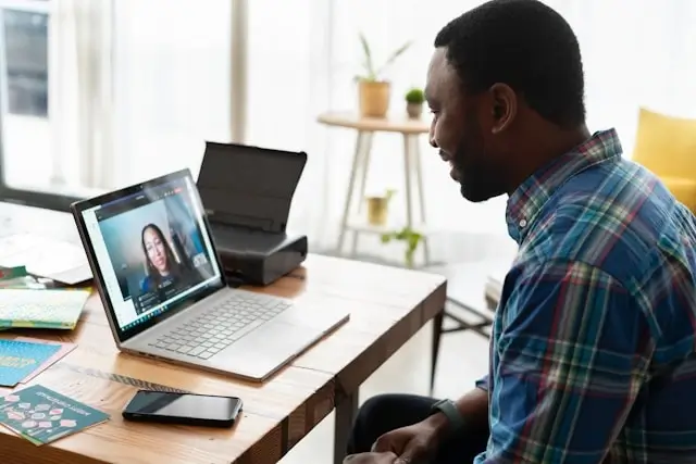 Man in plaid shirt participating in online law course via video call on laptop at home office desk, demonstrating remote legal education and virtual learning flexibility