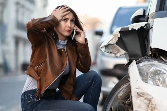 Distressed woman on phone next to damaged car after accident, illustrating the immediate aftermath and need for legal guidance in California car accident cases