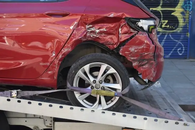 Severely damaged red car with crushed front end being loaded onto tow truck, demonstrating the type of property damage that leads to car accident lawsuits in California